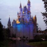 Disney After Hours: el castillo de Cenicienta de Magic Kingdom iluminado de azul y morado al anochecer, reflejado en el agua entre árboles