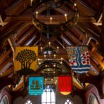 Disney Dining Plan: techo de madera de un salón de estilo medieval con lámparas de hierro con velas y estandartes de colores colgando sobre ventanas en arco