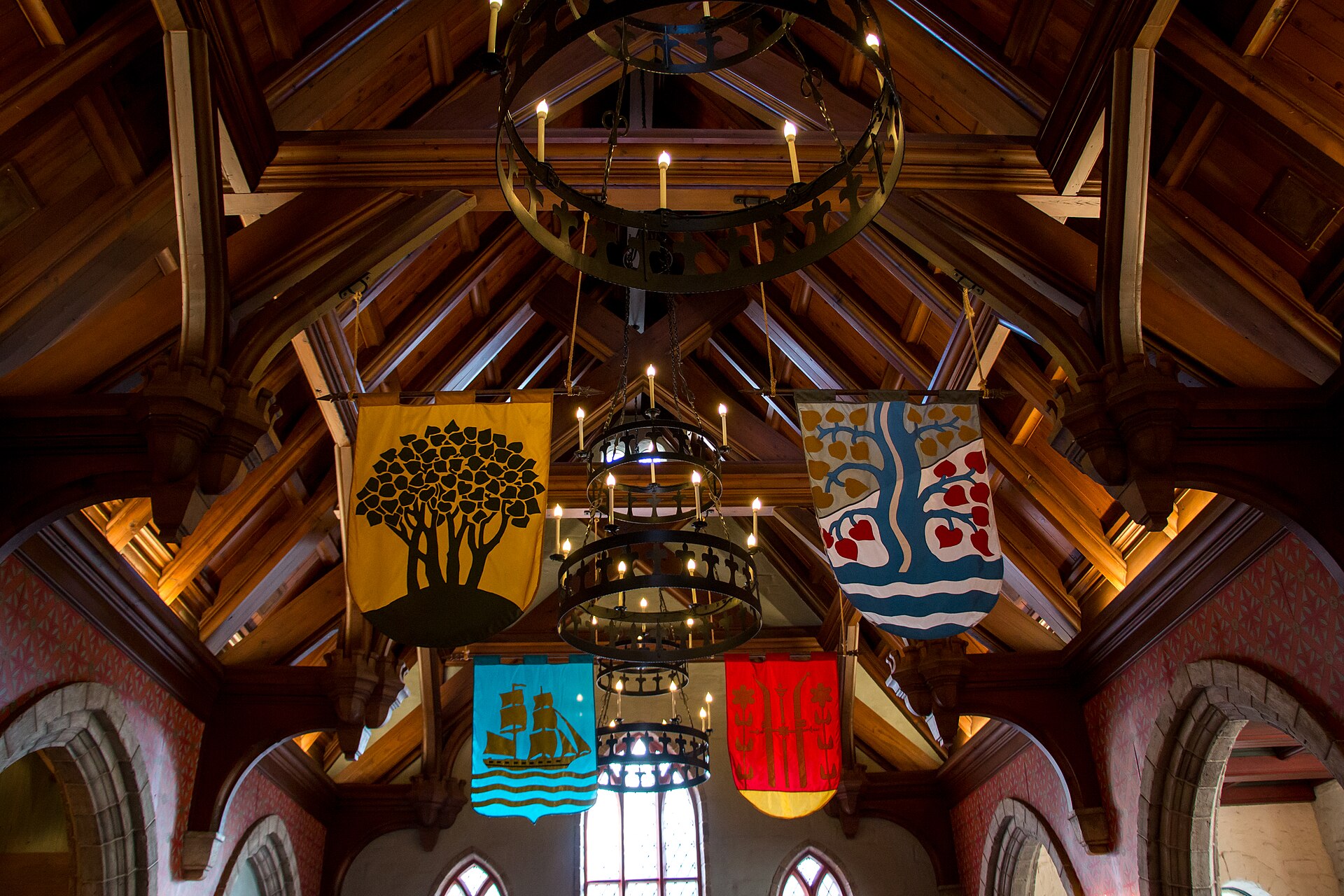 Disney Dining Plan: techo de madera de un salón de estilo medieval con lámparas de hierro con velas y estandartes de colores colgando sobre ventanas en arco
