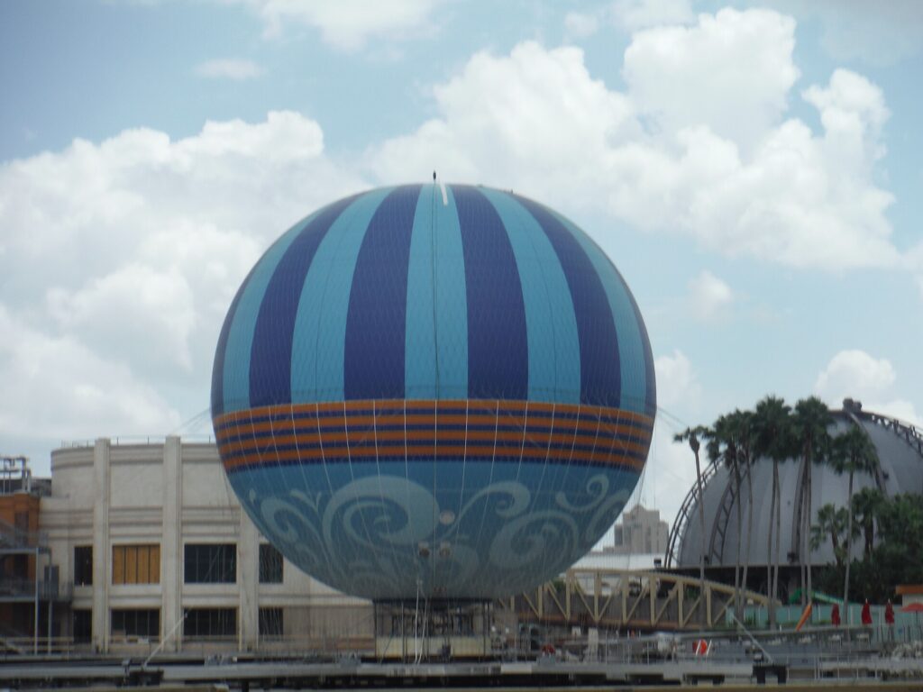 Globo cautivo azul y blanco Aerophile sobre el agua en Disney Springs, con palmeras y edificios al fondo