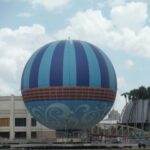Globo cautivo azul y blanco Aerophile sobre el agua en Disney Springs, con palmeras y edificios al fondo