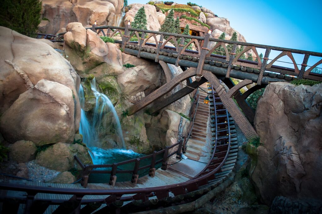 Early Theme Park Entry: vía de la montaña rusa Seven Dwarfs Mine Train con puentes de madera, rocas y una cascada en Magic Kingdom
