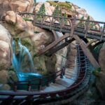 Early Theme Park Entry: vía de la montaña rusa Seven Dwarfs Mine Train con puentes de madera, rocas y una cascada en Magic Kingdom