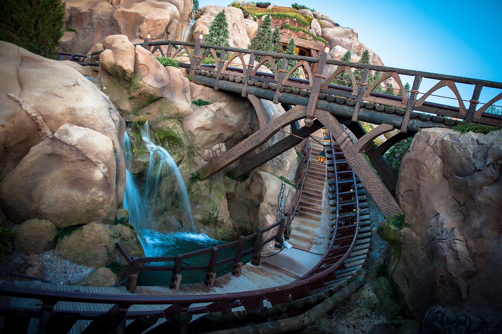 Early Theme Park Entry: vía de la montaña rusa Seven Dwarfs Mine Train con puentes de madera, rocas y una cascada en Magic Kingdom