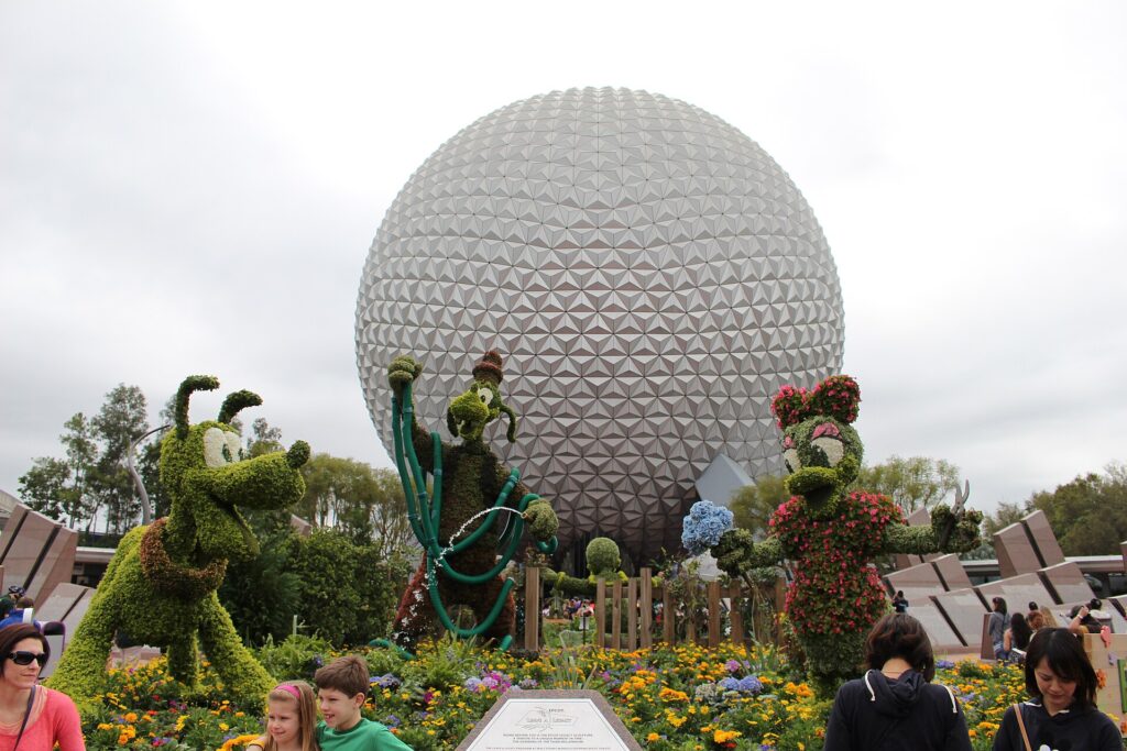 EPCOT Flower & Garden Festival: topiarios verdes de personajes de Disney junto a flores de colores frente a la esfera plateada de Spaceship Earth, con visitantes