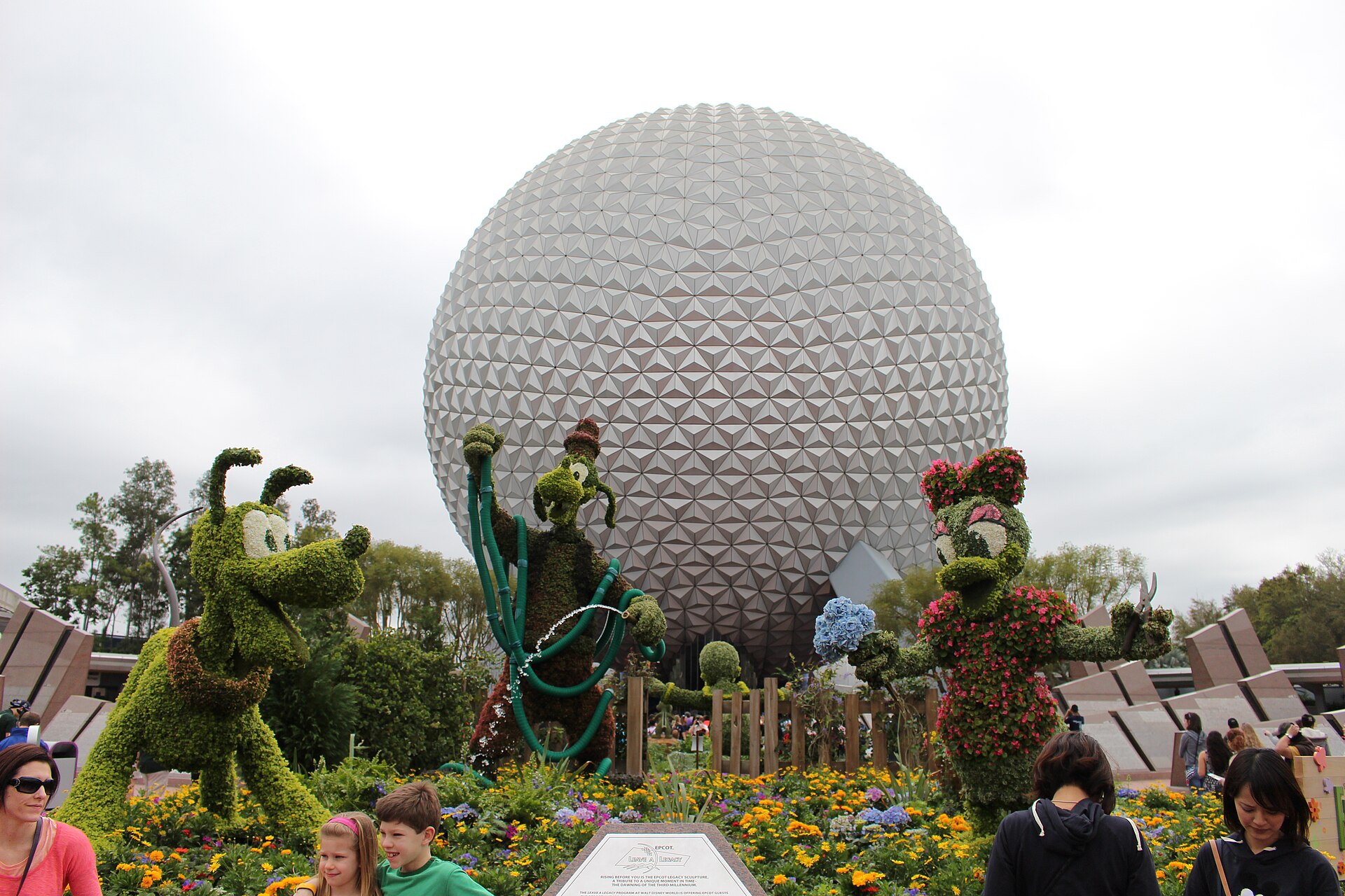 EPCOT Flower & Garden Festival: topiarios verdes de personajes de Disney junto a flores de colores frente a la esfera plateada de Spaceship Earth, con visitantes