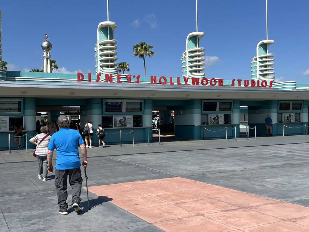 Hollywood Studios: entrada del parque con el letrero rojo de Disney's Hollywood Studios, torres blancas y verdes y visitantes caminando
