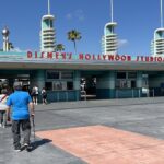 Hollywood Studios: entrada del parque con el letrero rojo de Disney's Hollywood Studios, torres blancas y verdes y visitantes caminando