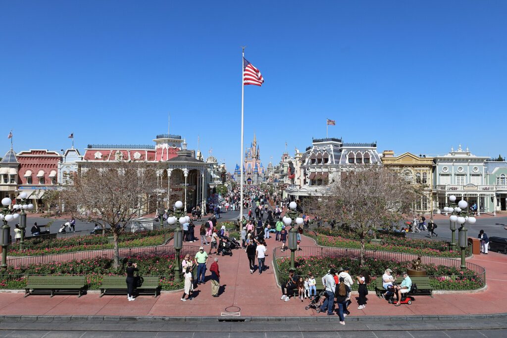 Main Street, U.S.A. en Magic Kingdom, con edificios de colores, jardines con flores, una bandera de EE.UU. y el castillo al fondo