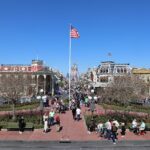 Main Street, U.S.A. en Magic Kingdom, con edificios de colores, jardines con flores, una bandera de EE.UU. y el castillo al fondo