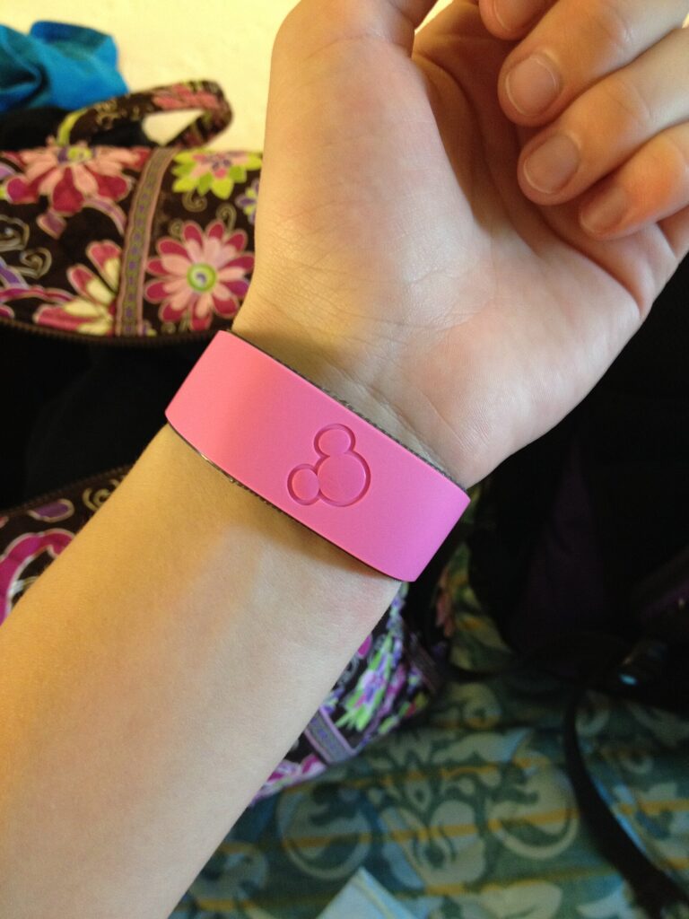 My Disney Experience: pulsera MagicBand rosada con el logo de Mickey en relieve, puesta en la muñeca de una persona
