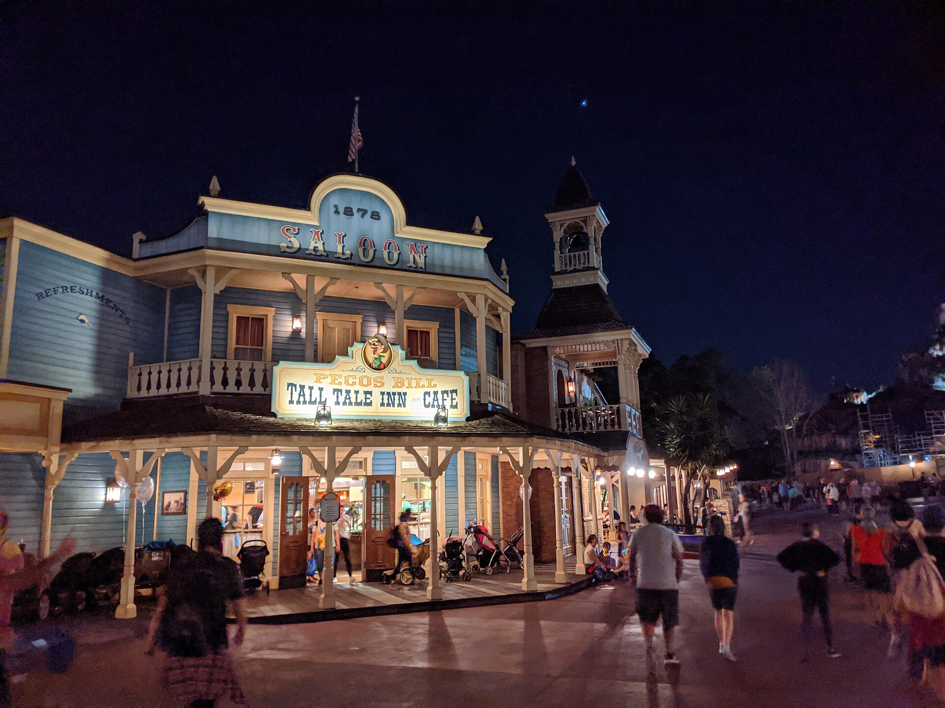 Mobile Order Disney: fachada iluminada de noche de Pecos Bill Tall Tale Inn and Cafe, local de comida rápida en Magic Kingdom