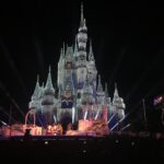 Very Merry Christmas Party: el castillo de Cenicienta cubierto de luces blancas de noche, con personajes vestidos de Navidad en un escenario y público delante
