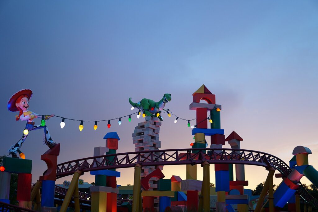 Rider Switch: la montaña rusa Slinky Dog Dash al atardecer, con una gran figura de Jessie, un dinosaurio verde, luces de colores y torres de bloques de juguete