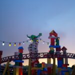 Rider Switch: la montaña rusa Slinky Dog Dash al atardecer, con una gran figura de Jessie, un dinosaurio verde, luces de colores y torres de bloques de juguete