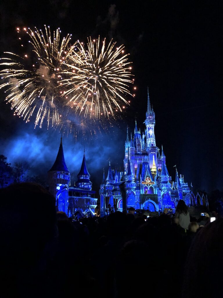 Shows nocturnos de Disney: fuegos artificiales dorados sobre el castillo de Cenicienta iluminado de azul, con siluetas del público en primer plano