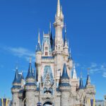 Virtual Queue en Disney Orlando: Castillo de Cenicienta en Magic Kingdom, con torres azules, un escenario al frente y visitantes bajo cielo azul