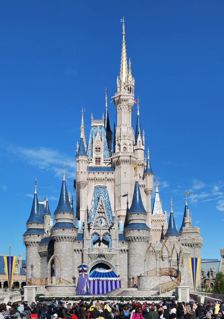 Virtual Queue en Disney Orlando: Castillo de Cenicienta en Magic Kingdom, con torres azules, un escenario al frente y visitantes bajo cielo azul
